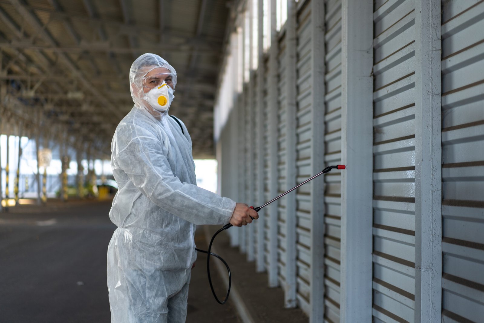 Worker wearing protective suit disinfection gear disinfect surface public place parking. Side view of disinfector safety overall and respiratory mask Covid pandemic disinfection preventive measures